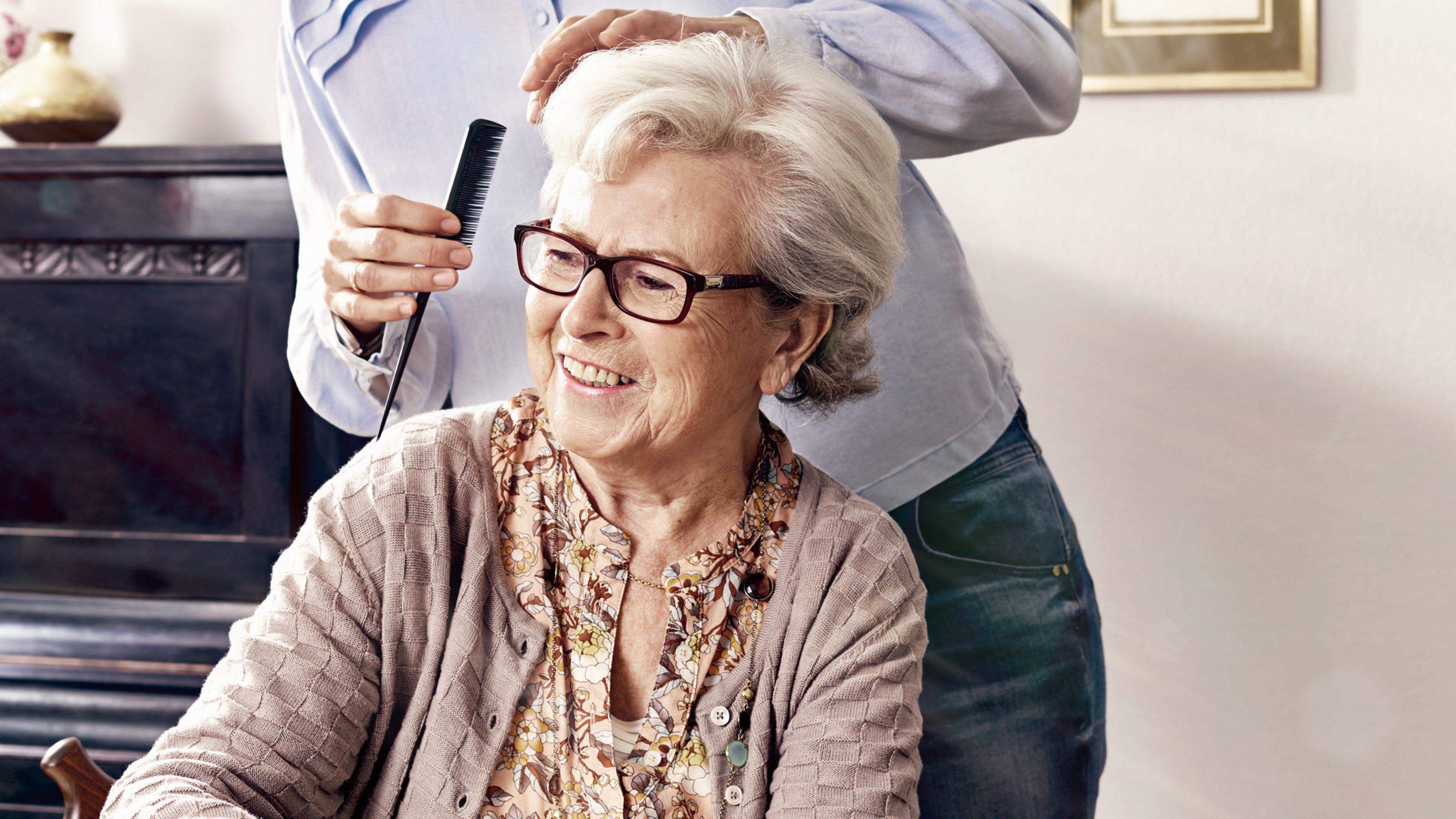 Pflegedienst kämmt einer Rentnerin die Haare.